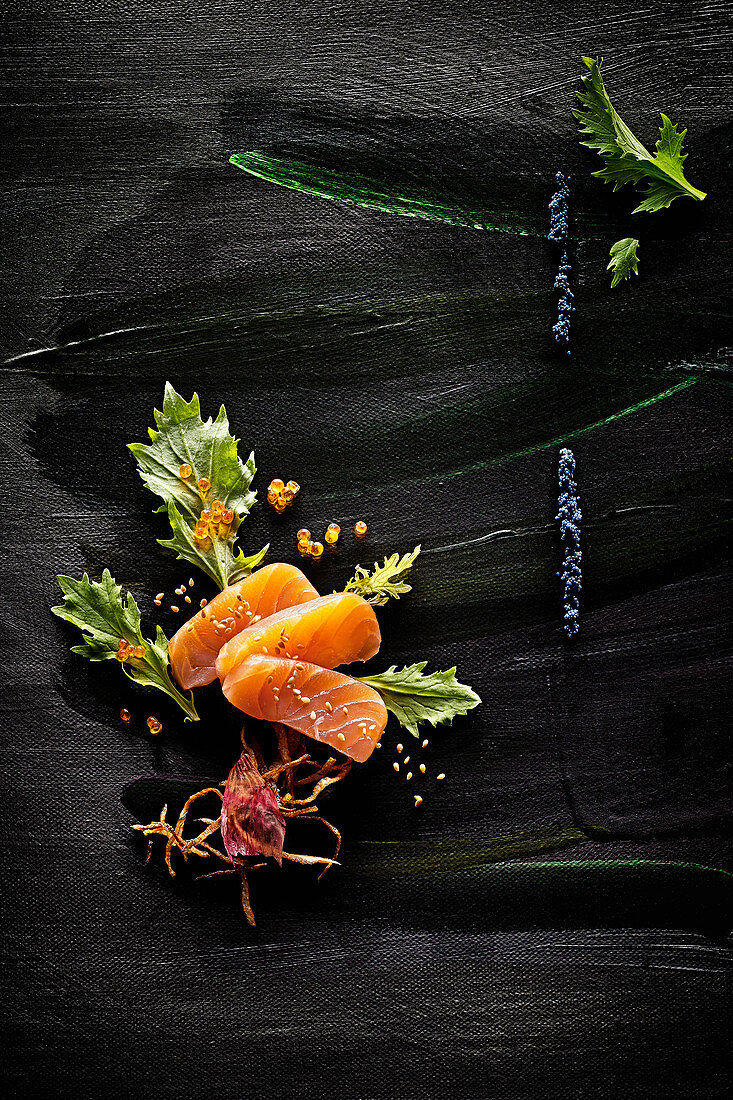 Food art: salmon with caviar, celery, roasted onions and sesame seeds on a black painted surface