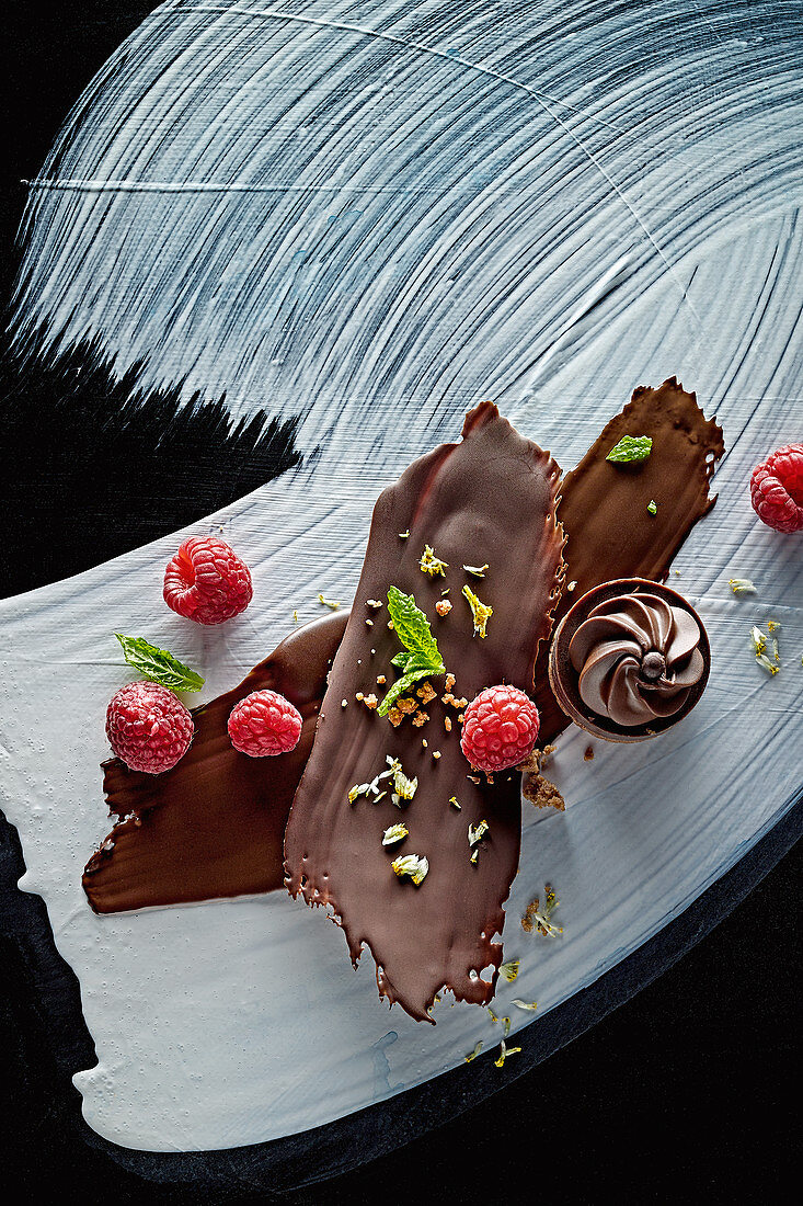 Food art: chocolate with raspberries, mint and chopped hazelnuts and nougat pralines on a painted surface