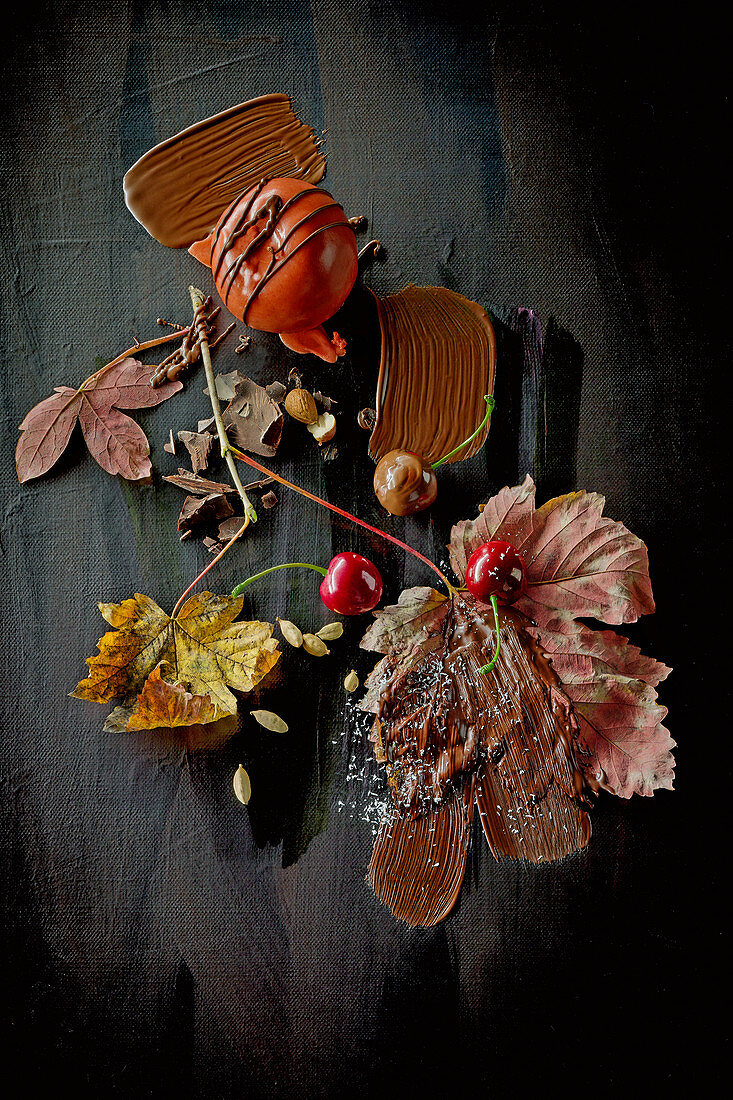 Food-Art: Winterapfel mit Schokolade, Kirschen und Herbstblättern auf schwarzem Untergrund