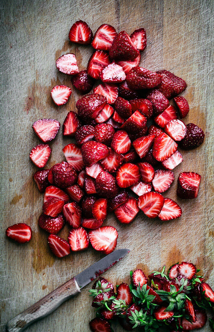 Erdbeeren, geputzt und geschnitten mit Messer auf Holzbrett (Aufsicht)