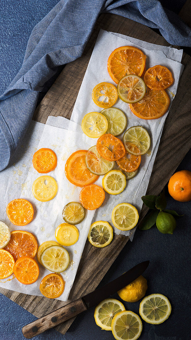 Candied orange, lemon and lime slices with a knife on a wooden cutting board