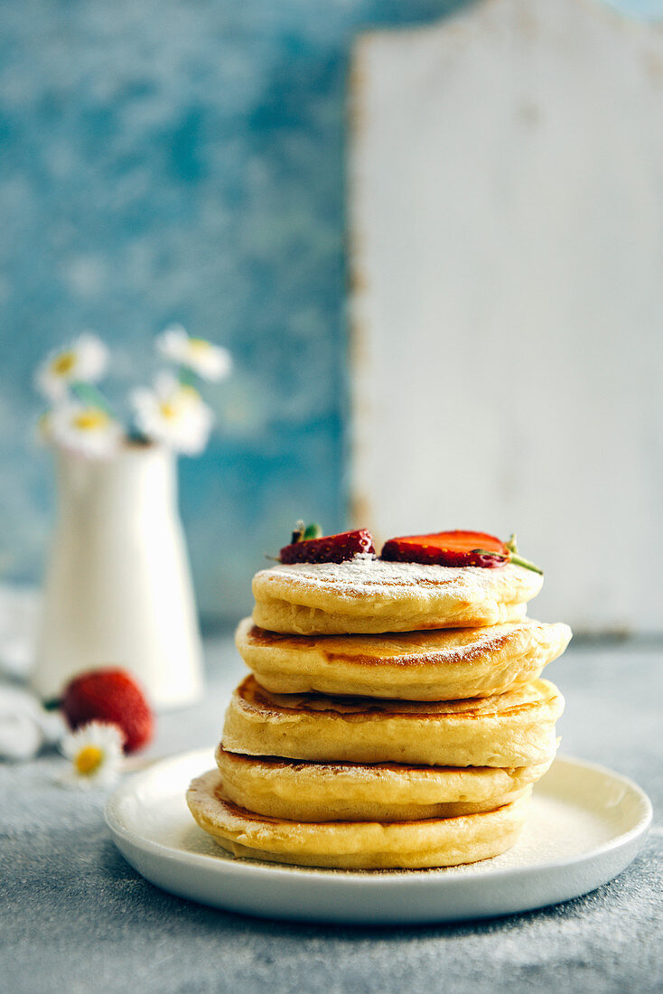 Almond milk pancakes topped with strawberries and powdered sugar stacked