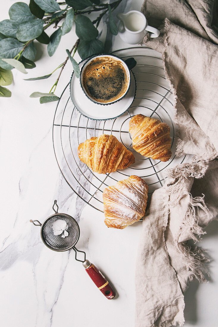 Croissants mit Puderzucker und einer Tasse Kaffee auf Abkühlgitter