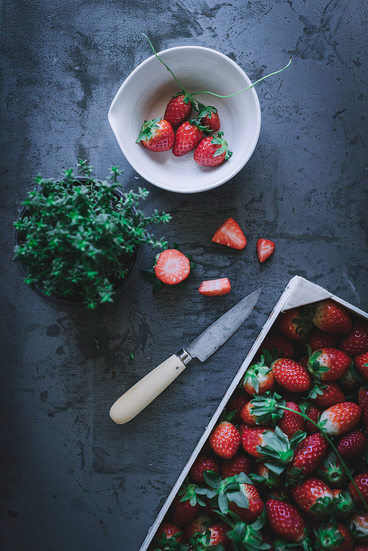 Stillleben mit Thymian und frischen Erdbeeren in Kiste und Schälchen (Aufsicht)