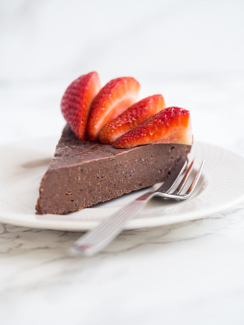 Ein Stück mehlloser veganer Schokoladen-Fudge-Kuchen mit Erdbeeren