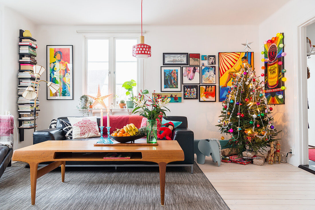 Coffee table in front of black leather sofa in living room with Christmas tree in corner and comic-style artworks on wall