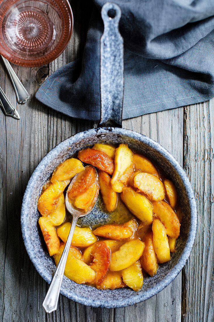 Cooked peaches in a skillet on a wooden background