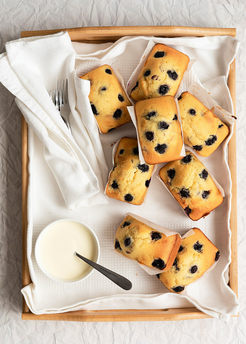 Individual blueberry loaf cakes with a bowl of cream on a wooden tray