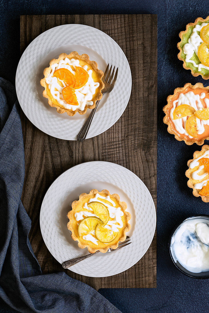 Lemon tarts on plates alongside a bowl of yoghurt and a lime and orange tart