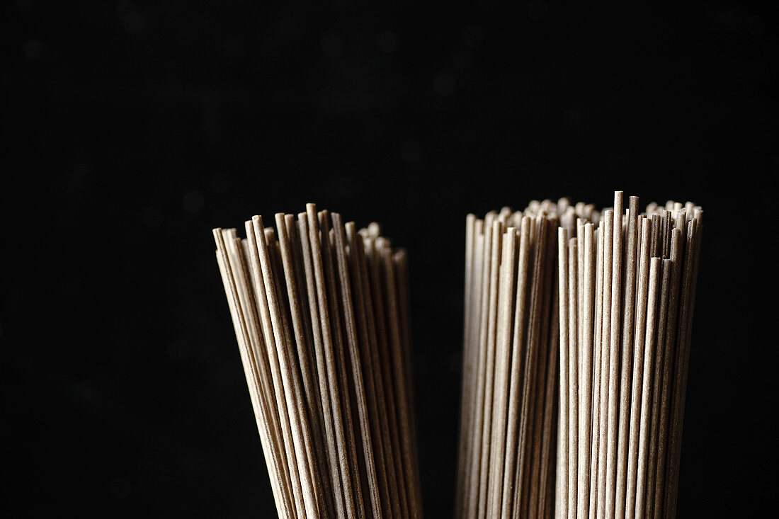 Close up of soba noodles, bamboo steamer and asian cuisine props on dark background