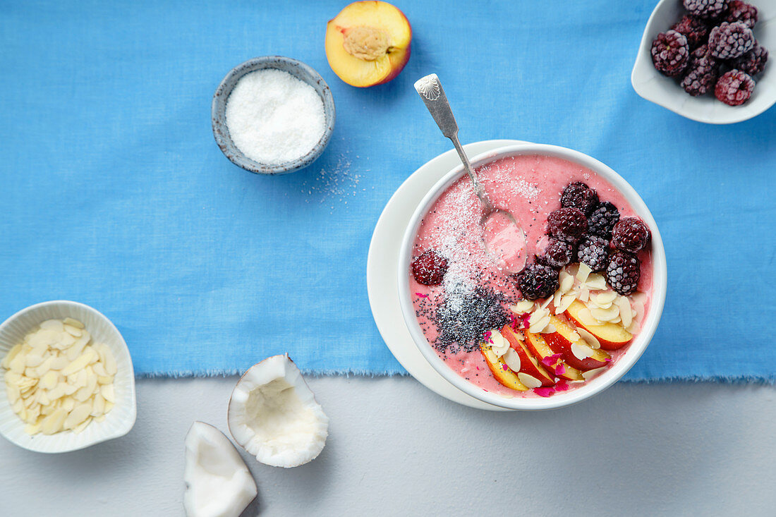 Fresh and cold strawberry banana smoothie garnished with peach slices, frozen blackberry, chia seeds and almond flakes