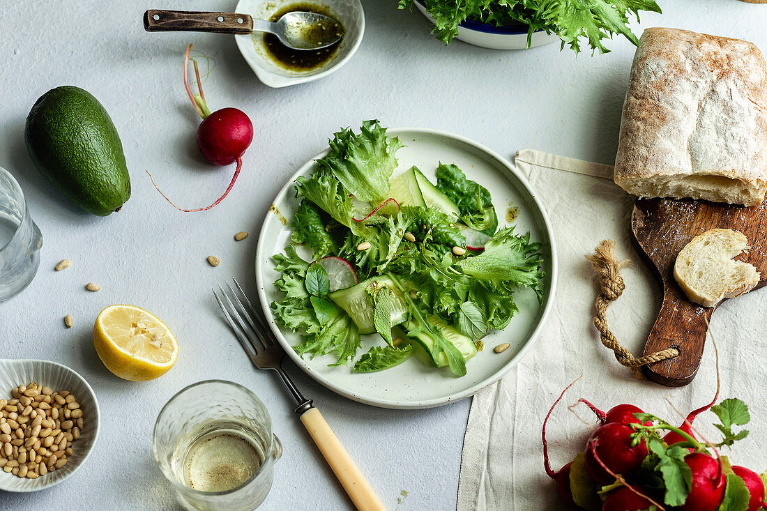 Frischer grüner Blattsalat umgeben von Zutaten und Brot (Aufsicht)