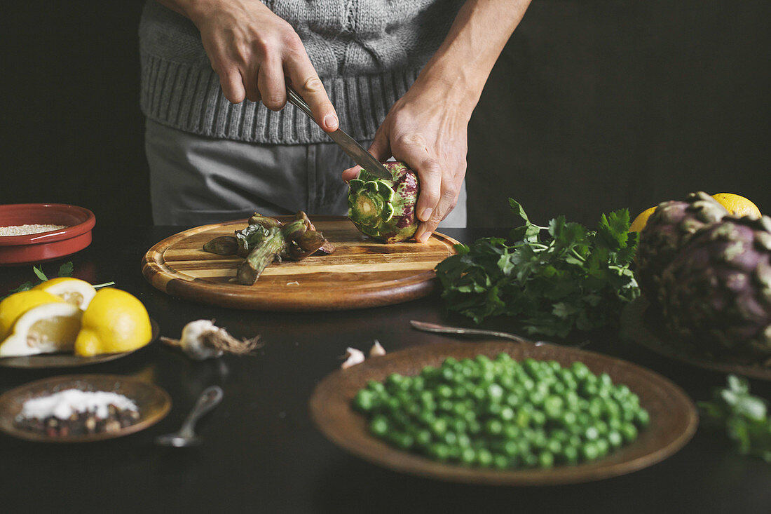 A man prepares lunch with artichokes and peas