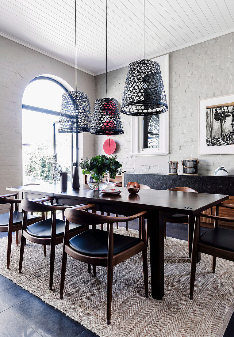 Dark dining table with chairs, hanging lamps from old fishing baskets in the room with a white-painted brick wall