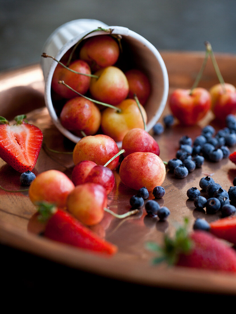 Rainier cherries, strawberries and wild blueberries on a copper tray and in a white tin cup