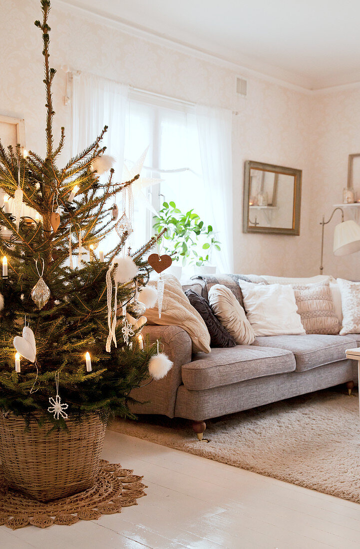 Geschmückter Weihnachtsbaum neben grauem Polstersofa im Wohnzimmer