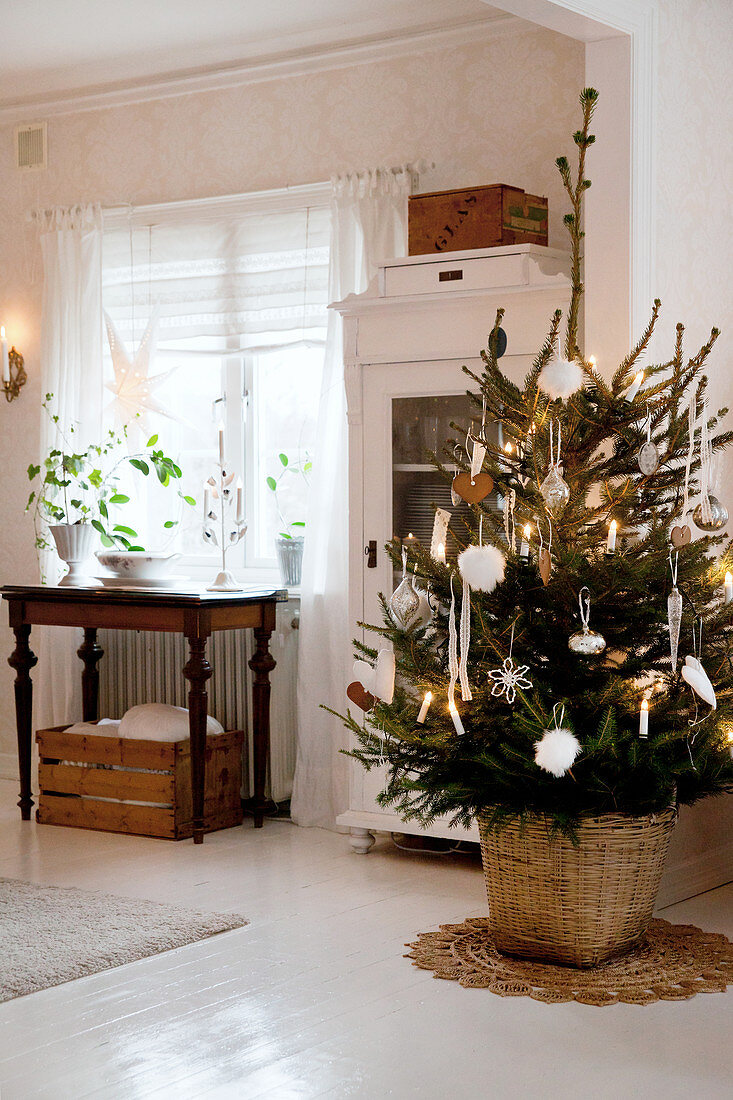 Decorated Christmas tree in front of glass-fronted cabinet in Scandinavian dining room with white wooden floor