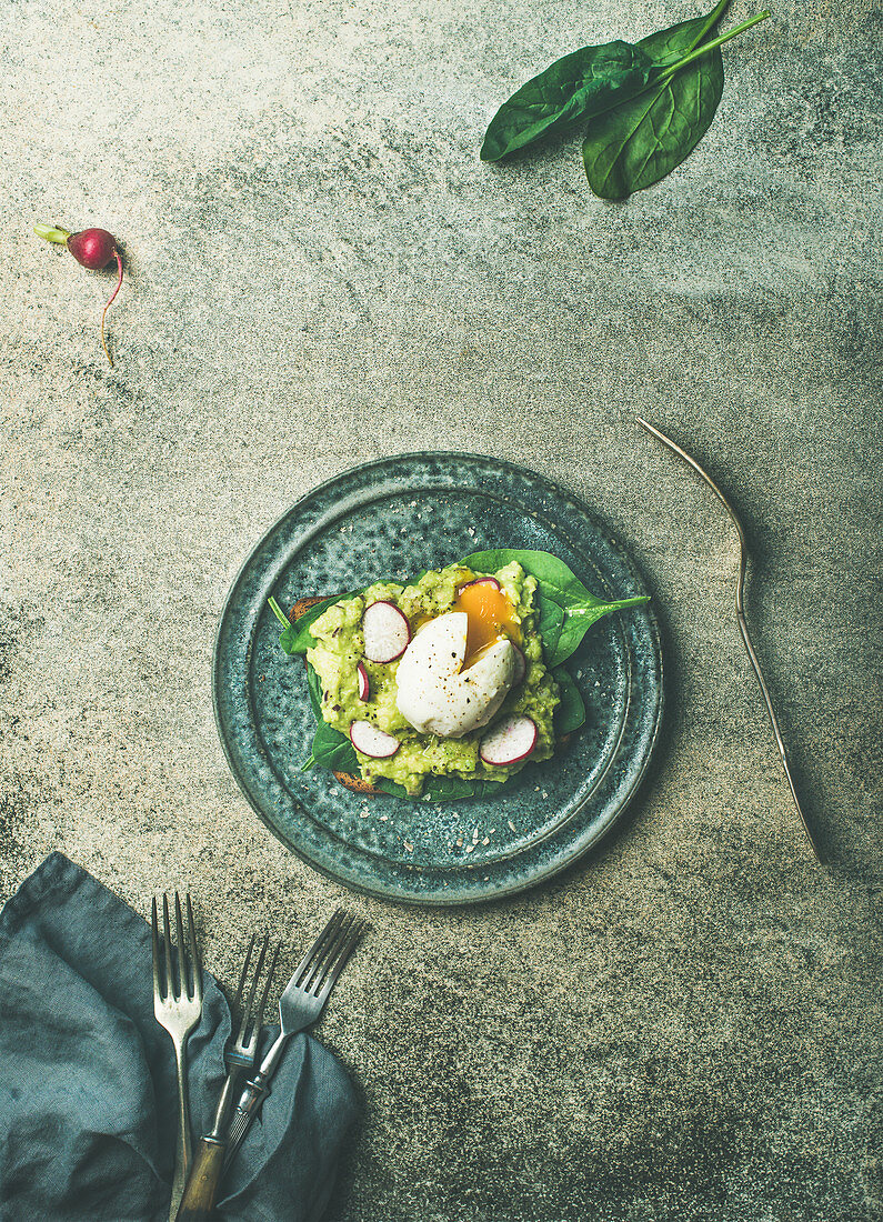 Wholegrain toasts with avocado, spinach and poached egg on plate over grey concrete background