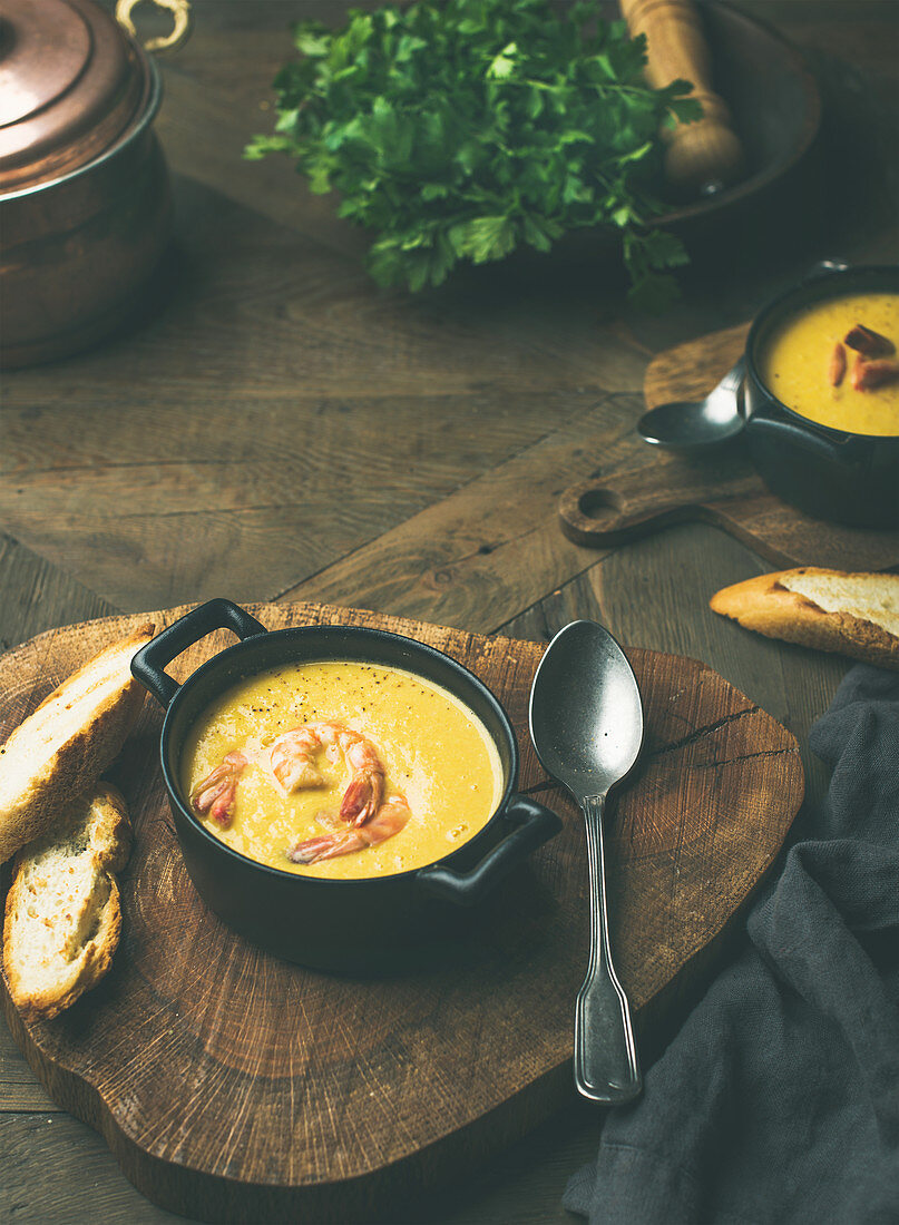 Corn creamy soup with shrimps served in individual pots with bread over rustic dinner table