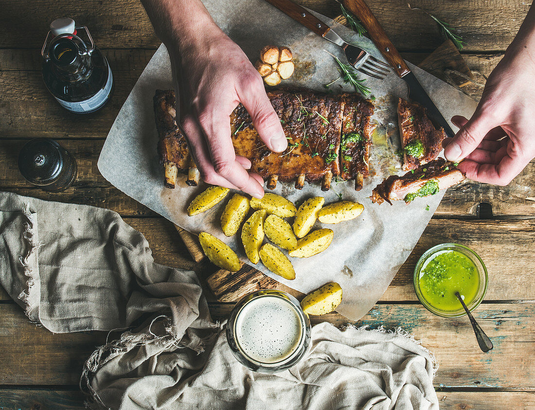 Man eating roasted pork ribs with garlic, rosemary, fried potato and green herb sauce