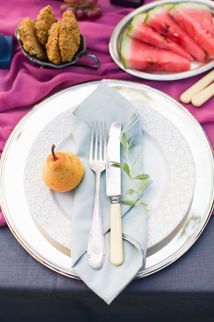 Pear, cutlery and folded napkin on plate