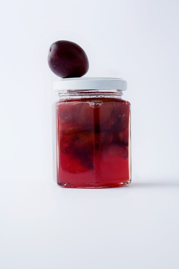A glass of plum jam against a white background