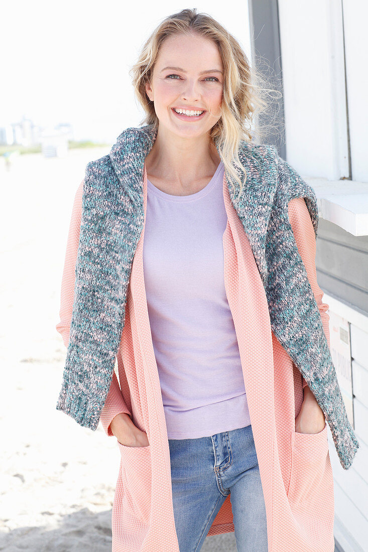 Blonde Frau in lila T-Shirt, apricotfarbener Jacke und Pulli über den Schultern