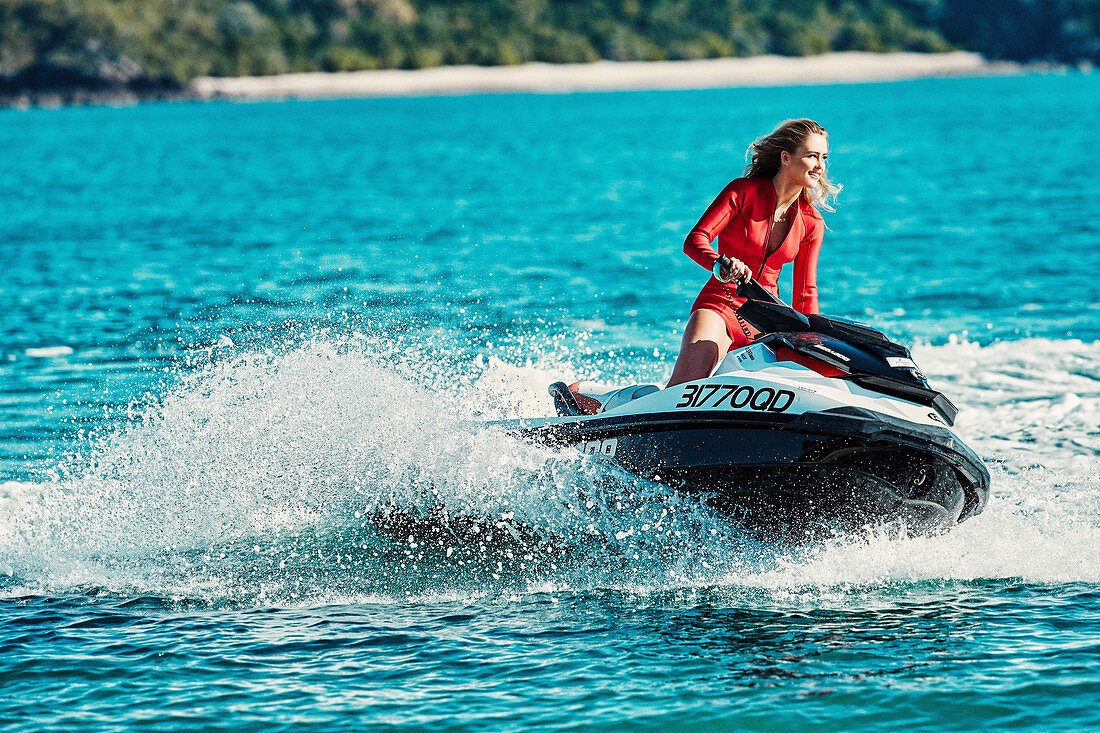 A young woman wearing a red neoprene wetsuit on a jetski