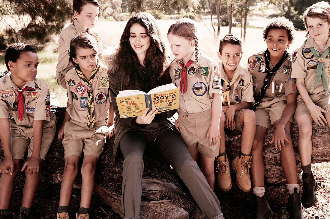 A dark-haired woman reading to children in uniform