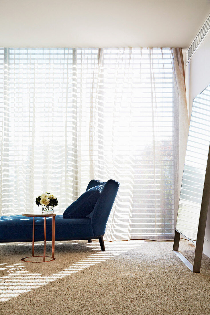 Dunkelblaue Chaiselongue und Beistelltisch mit Blumen vor Fenster im Schlafzimmer