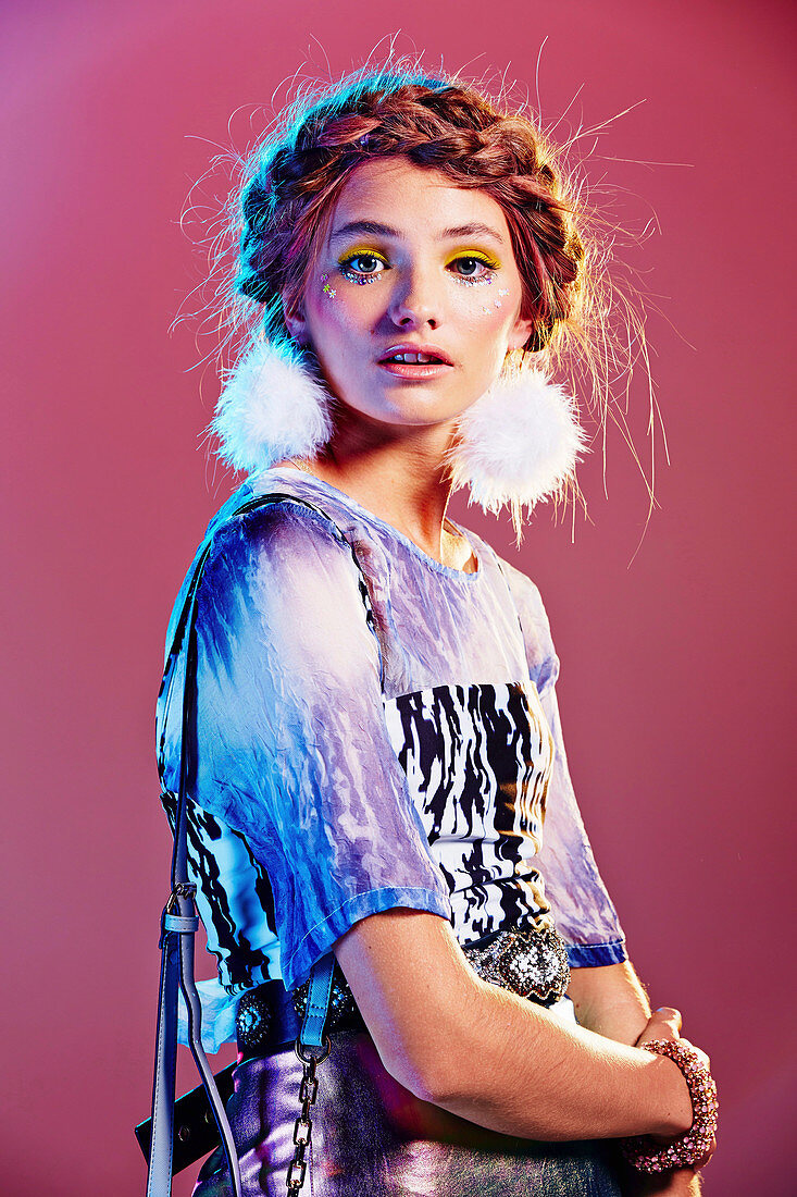 A girl with a plaited hairstyle, pompom earrings and glittery make-up