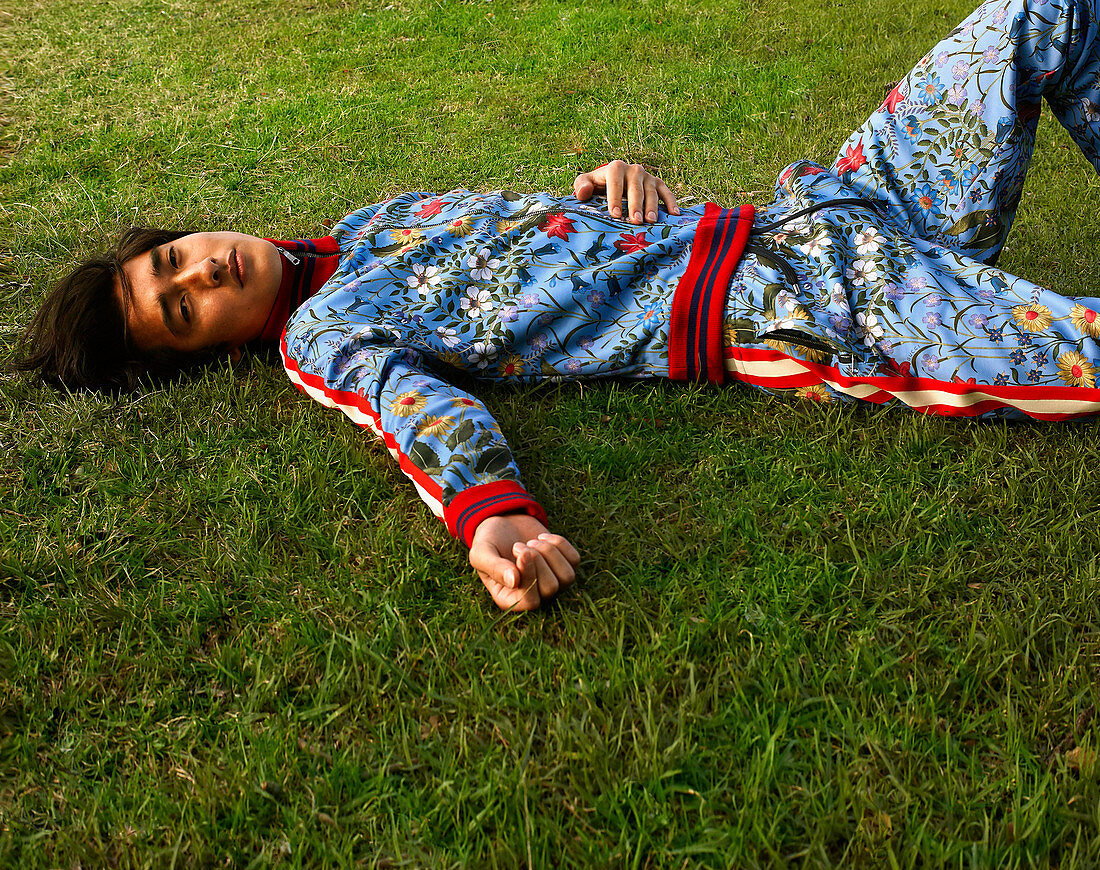 A young man wearing a floral-patterned tracksuit lying on the grass