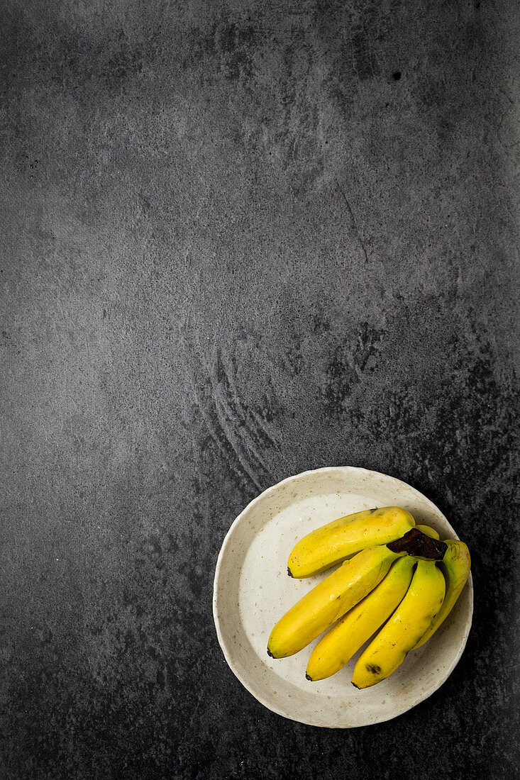 Small bananas on a white plate at a black backdrop