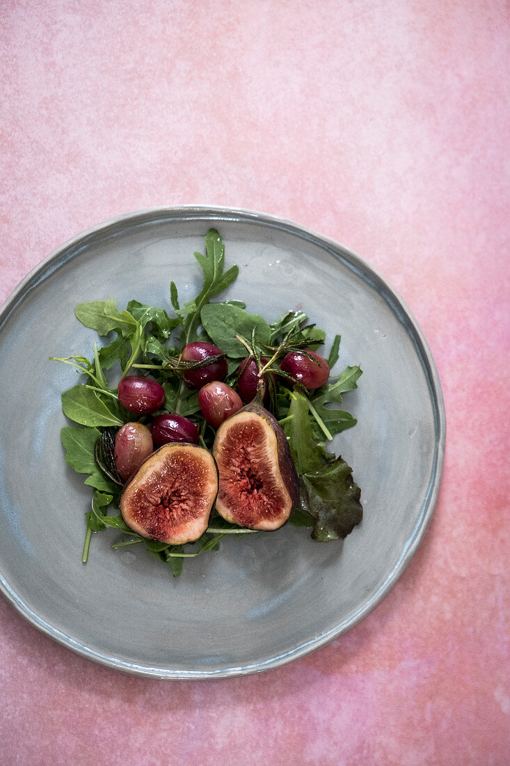 A salad with figs, garpes and lettuce on a grey plate on a pink backdrop