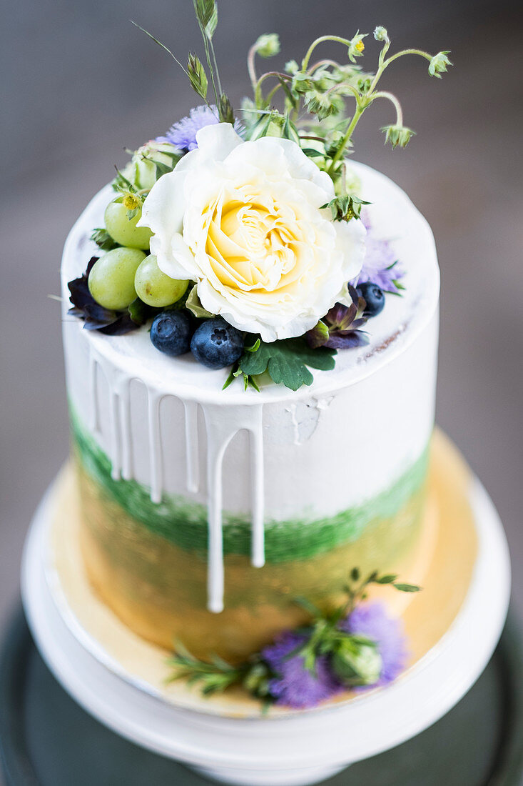 A layered cake with gold, green, grapes and flowers