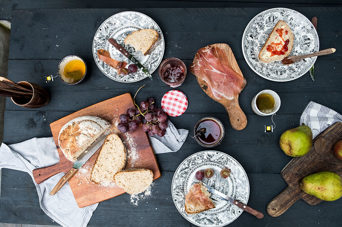 Lunch with bread, grapes, pears, cups of tea, marmelade and jambon