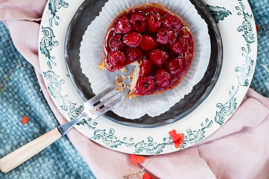 Raspberries tartelette with a fork on a old playe and a pink napkin