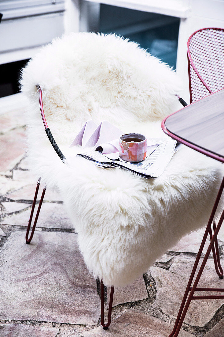 Tasse und Zeitschrift auf einem Stuhl mit Schaffell