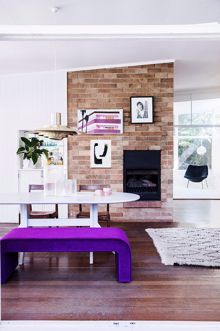 Violet upholstered bench at the dining table in front of the brick fireplace