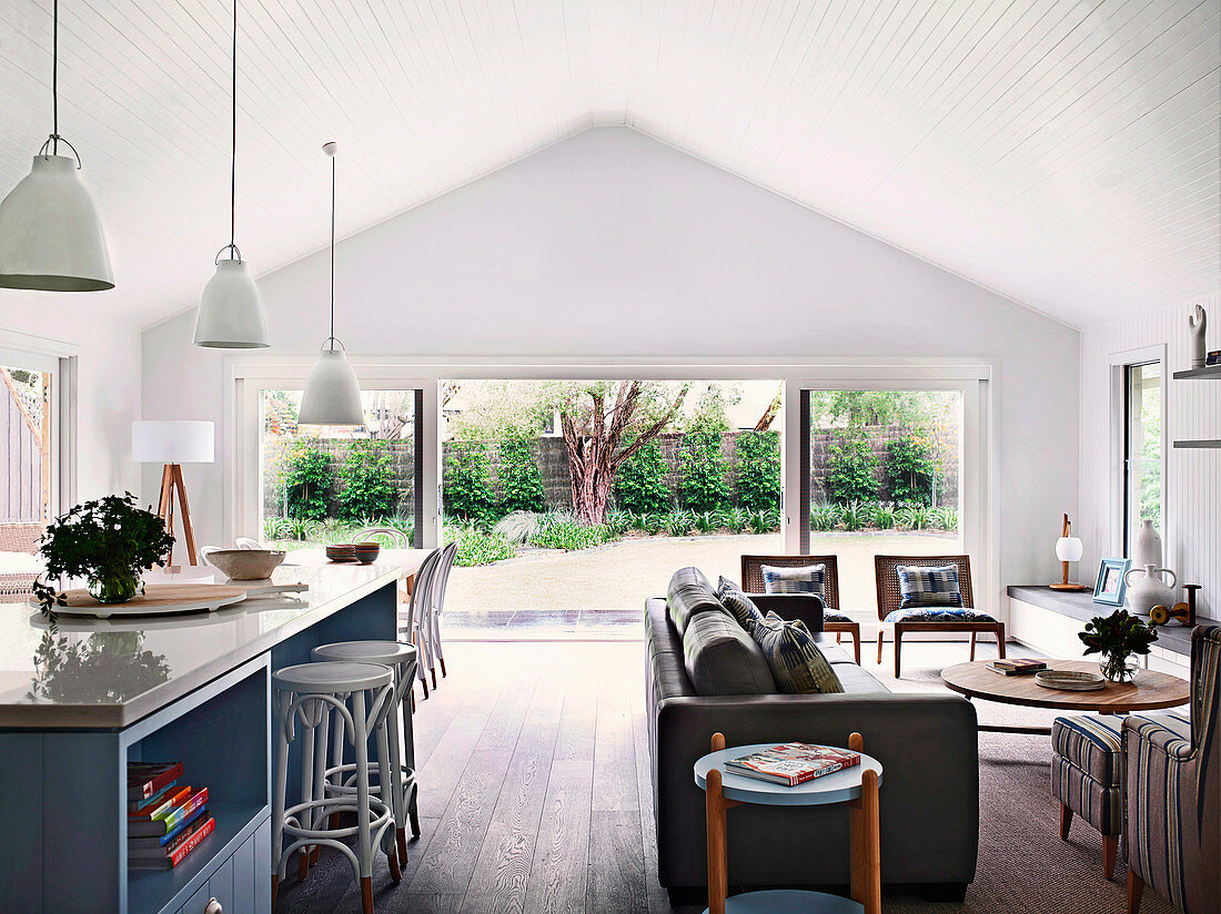 Kitchen island with bar stools and lounge with leather sofa and rattan chairs in an open living room with terrace access