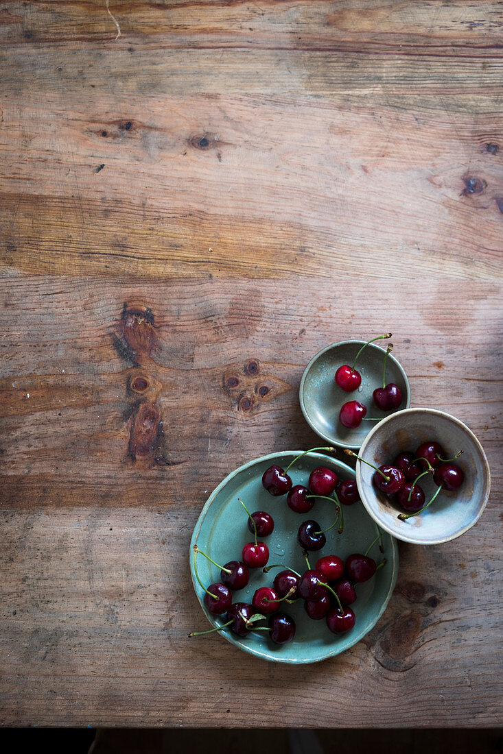 Cherries on three green plates at a wooden table