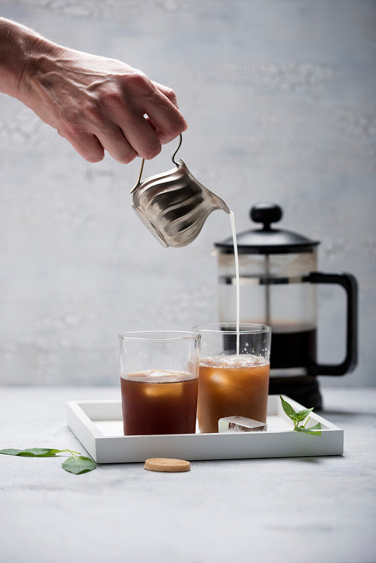 A woman pouring almond milk into iced cold brew coffee