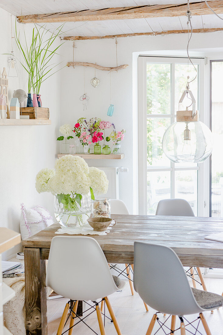Weiße Hortensien auf rustikalem Holztisch, darüber Pendelleuchte mit Glasschirm und Klassikerstühle im Esszimmer