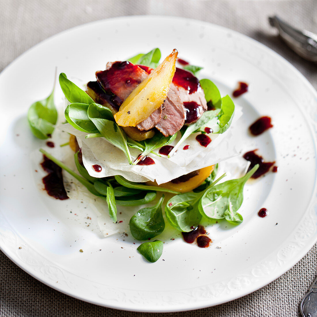 Duck breast roasted with pear, salad on a white plate