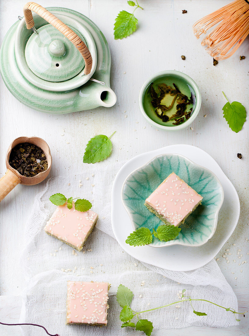 Matcha green tea cakes with white chocolate glaze and sesame seeds with a cup of green tea and balm, mint leaves.
