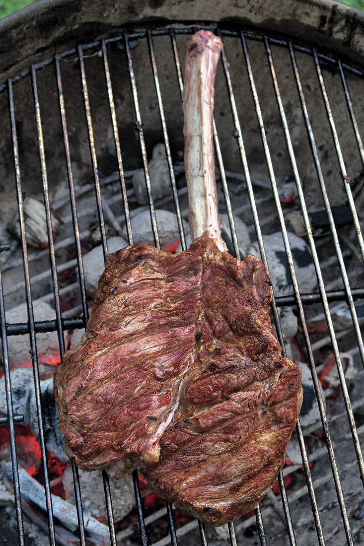 A veal tomahawk steak on a grill over a fire (top view)