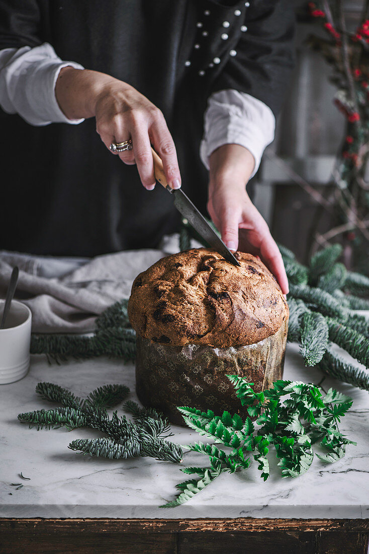 Crop person cutting fresh baked tasty Panettone on kitchen table