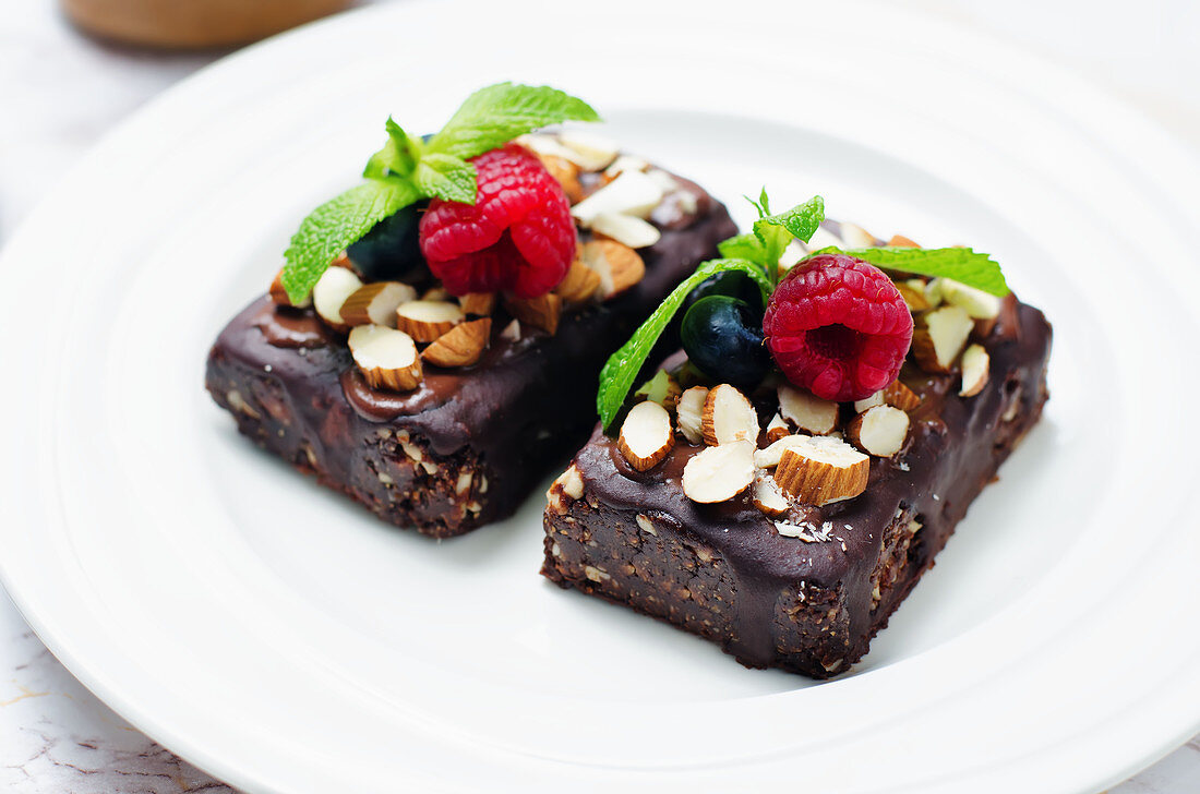 Raw vegan no bake chocolate, dates and almond brownies with chocolate frosting and berries