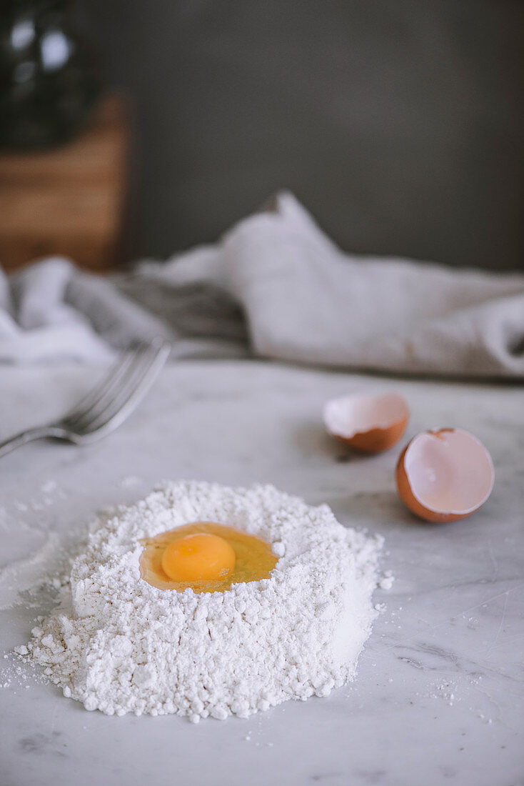 Raw egg lying on heap of flour on marble tabletop