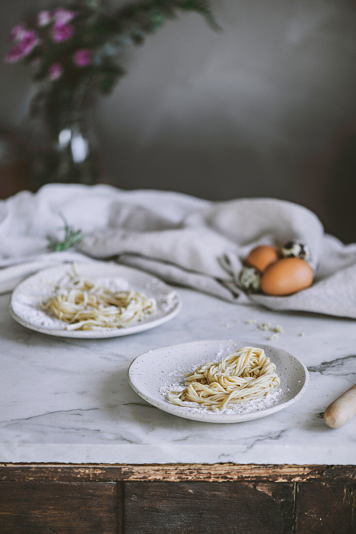 Rohe selbstgemachte Pasta auf Tellern und rustikalem Küchentisch